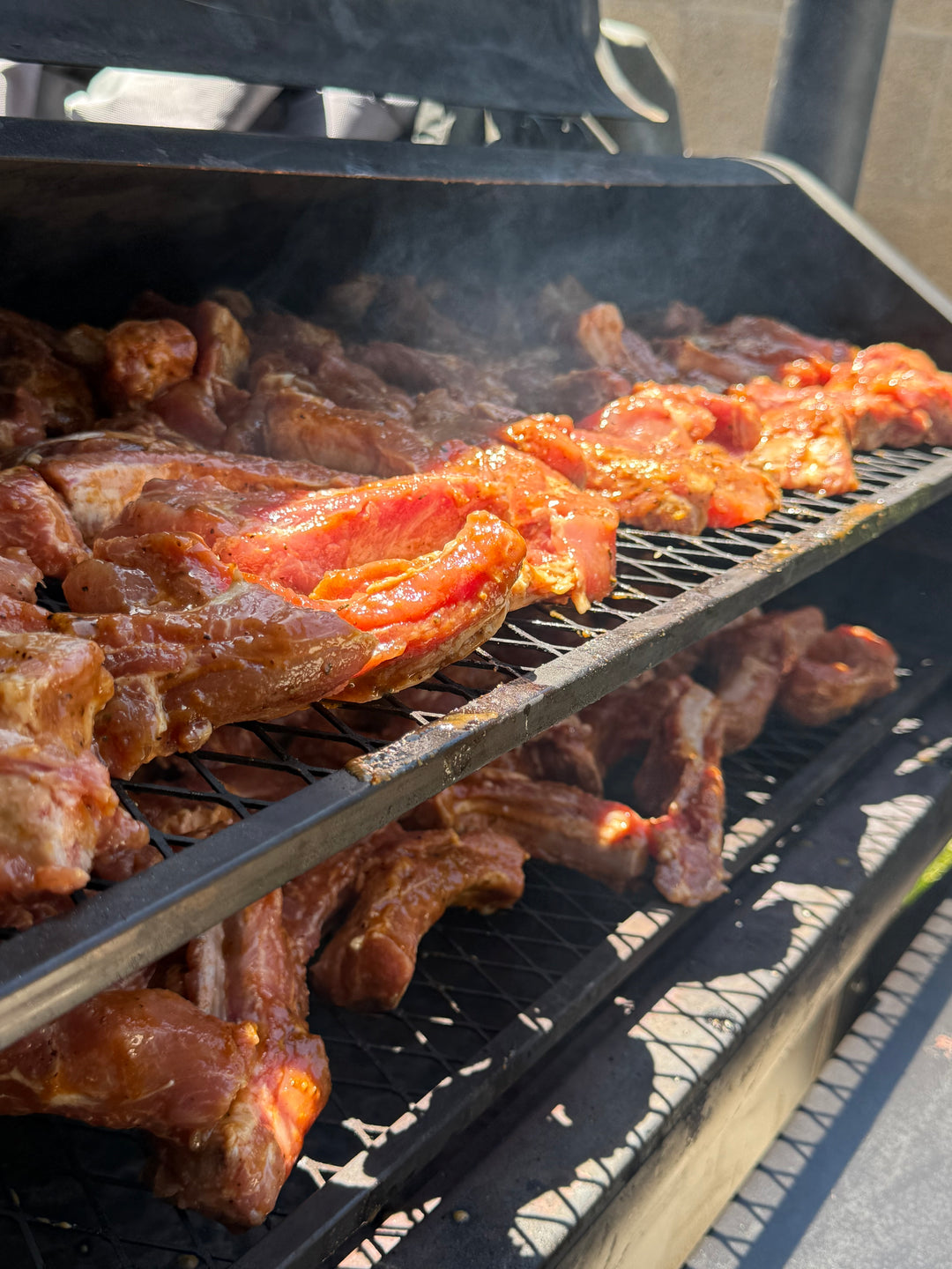 Pork ribs seasoned with BuffalowBBQ Sassy Swine BBQ Rub smoking on an outdoor grill.